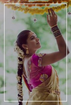 a woman in a pink and yellow sari holding her hands up to the sky