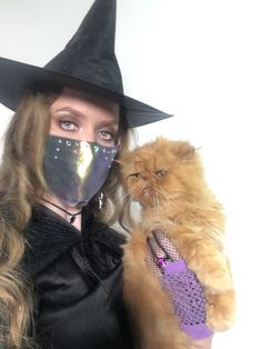 a woman in a witch costume holding a cat and wearing a mask on her face