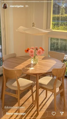 a wooden table and chairs with flowers in a vase on the table next to a window