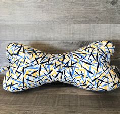 a dog bone pillow with an abstract design on the front and back, sitting against a wooden wall