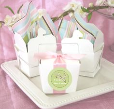 small white boxes with pink bows on them sitting on a plate next to some flowers