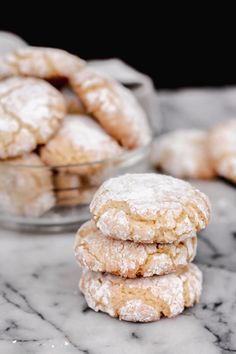 a stack of powdered sugar cookies sitting on top of a marble counter next to a glass bowl