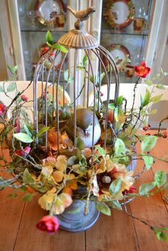 a birdcage filled with flowers and leaves on top of a wooden table