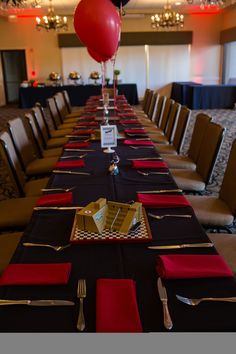 a long table is set with red and black napkins, silverware, and balloons