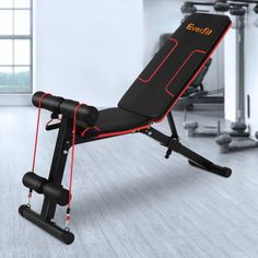 a black and red exercise bench in a room with other equipment on the wall behind it