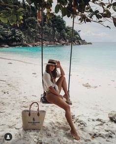 a woman sitting on a swing at the beach with her handbag in front of her face