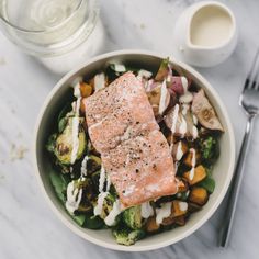 a bowl filled with salmon and vegetables next to a glass of water