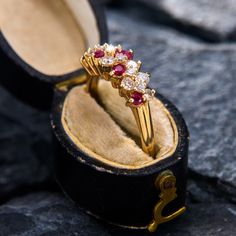 a gold ring with red and white stones sits in an open box on the ground