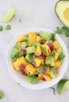 an avocado and mango salad in a white bowl with limes around it