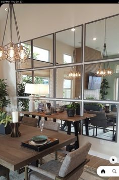 a dining room table and chairs with mirrors on the wall behind them, in front of a large window