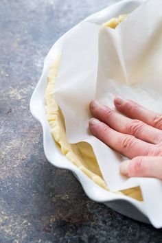 a person's hand on top of a pie crust in a white dish with parchment paper