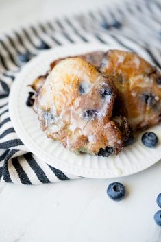 two blueberry donuts on a white plate with black and white striped napkins