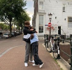 two people hugging each other in front of a building with bicycles parked on the sidewalk