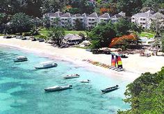 a beach with several boats in the water and houses on the other side, surrounded by trees