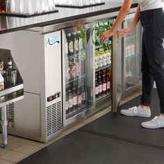 a woman standing in front of a cooler filled with drinks and sodas next to a counter