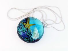 If you love the ocean, you can't help but love this unique pendant of ours, which represents the seabed. Handcrafted from beautiful olive wood and blue clear epoxy resin, this pendant captures the serene beauty of the marine world, with starfish and shells within the resin. It is the perfect accessory for anyone who loves the sea. Whether you're searching for a unique birthday gift or looking to add a touch of the ocean to your outfit, this ocean-inspired pendant is the perfect choice. Its disti Blue Resin Ocean-inspired Necklaces, Blue Resin Necklaces With Ocean-inspired Style, Ocean-inspired Turquoise Round Pendant Necklace, Blue Resin Ocean-inspired Necklace, Ocean-inspired Blue Resin Jewelry, Blue Ocean-inspired Resin Jewelry, Ocean-inspired Blue Pendant Necklace, Marine World, Sea Necklace