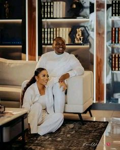 a woman sitting on top of a white couch next to a man in a black suit