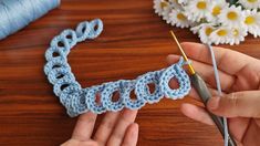 someone is crocheting a piece of blue yarn on a table with flowers in the background