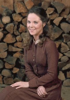 a woman sitting on top of a pile of logs wearing a brown shirt and skirt