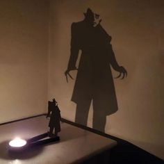 a shadow of a man standing next to a table with a light on it and a toy in front of him