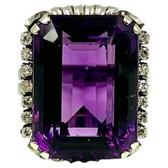 Fine, large Art Deco period Amethyst and Diamond ring in a beautifully detailed 18K white gold setting. Early 20th Century The amethyst, measuring approximately 22.5 carats, lively rich purple color. 14 single cut diamonds, seven on each side of the amethyst, approximately .3TCW Substantial, stylish setting marked 750 for 18K gold on the interior of band. Very good condition commensurate with age, a few very slight nicks observerved under 10X magnification 22mm by 19mm front measurements Size 6. Amethyst And Diamond Ring, Gold Cocktail Ring, Gold Cocktail, Art Deco Period, Large Art, Eiffel Tower Inside, Cocktail Rings, White Gold Rings, Early 20th Century