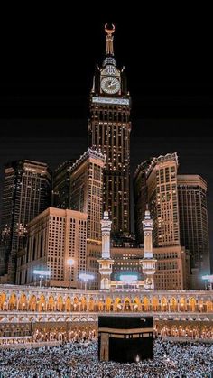 a large group of people standing in front of a clock tower with lights on it