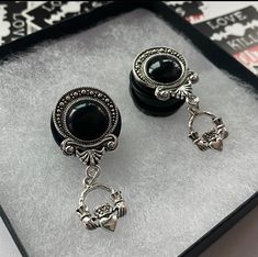 a pair of black earrings sitting on top of a silver tray next to each other