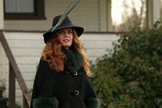 a woman wearing a black coat and green fur collar with a hat on her head