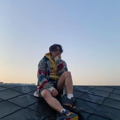 a young man sitting on top of a roof drinking from a cup in his hand