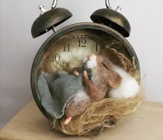 an old fashioned alarm clock with stuffed animals in it's nest on a wooden table