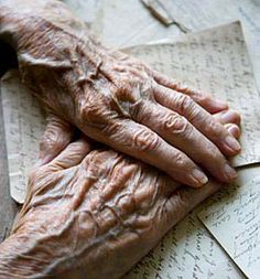 an old woman's hands resting on top of some paper with writing around it