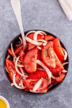 a black bowl filled with sliced tomatoes and onions next to a small cup of mustard