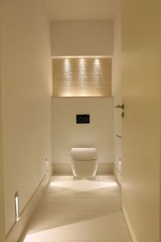 a white bathroom with a toilet and lights on the wall above it's tank