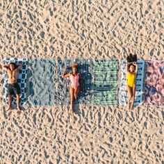 three people laying on beach towels in the sand with their backs turned to the camera