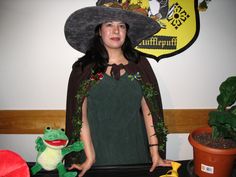 a woman wearing a green dress and black hat standing in front of a table with stuffed animals