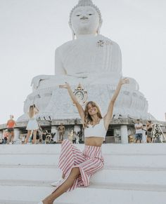 a woman sitting on steps in front of a large buddha statue with her arms up