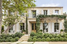 a large white house with lots of windows and plants on the front lawn, along with steps leading up to it