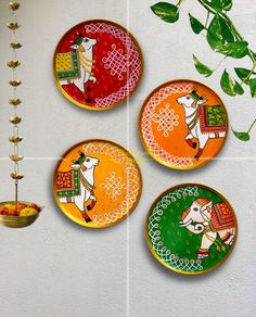 four colorful plates are hanging on the wall next to a potted plant and vase