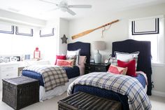 two beds in a bedroom with plaid comforters and pillows on them, one has a basket under the headboard