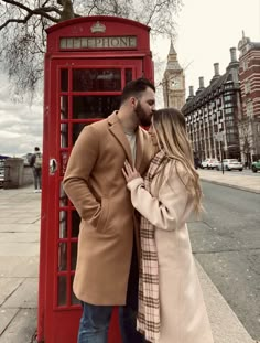 a man and woman standing next to a red phone booth