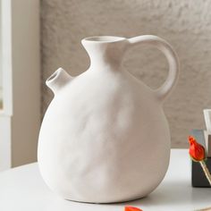 a white vase sitting on top of a table next to a book and flower pot