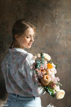 a woman holding a bouquet of flowers in front of a gray wall with peeling paint