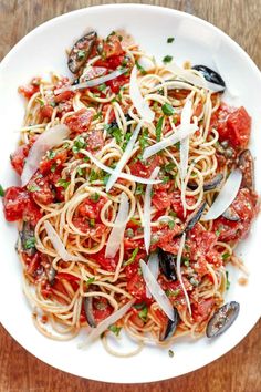 a white plate topped with pasta and clams on top of a wooden table next to a fork