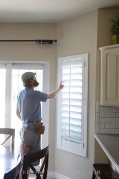 a man standing in front of a door pointing at the window with shutters open