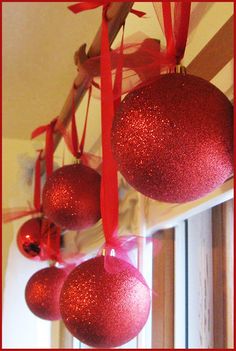 three red ornaments hanging from the ceiling in front of a window with ribbon on them