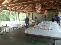 people are standing around tables with white tablecloths and orange decorations hanging from the ceiling