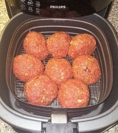 some meatballs are sitting in an air fryer on the counter top, ready to be cooked