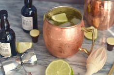 a copper mug filled with liquid and limes on a marble table next to bottles