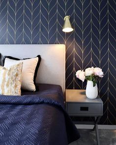 a bed with blue sheets and pillows next to a night stand with flowers on it