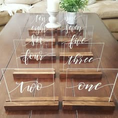 four clear acrylic signs sitting on top of a wooden table next to a candle